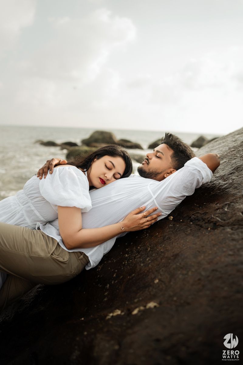 A tender moment captured of a couple resting together on coastal rocks by the ocean.