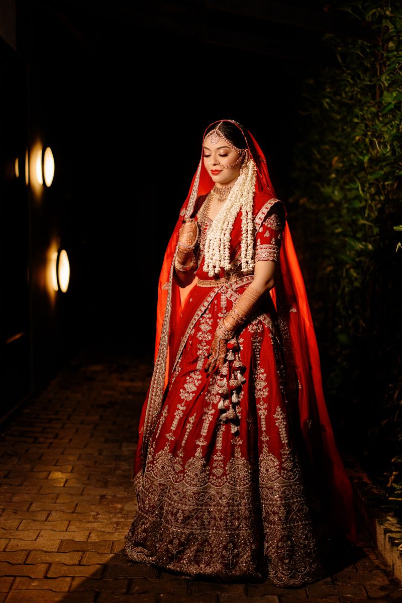 Traditional Indian bride wearing an ornate red lehenga with intricate embroidery and jewelry in an evening setting.