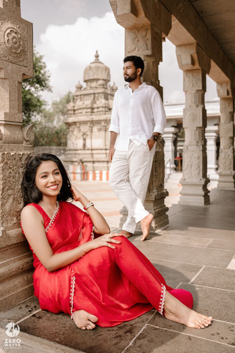 Couple relaxes under a stone colonnade with traditional Indian architecture visible in background.