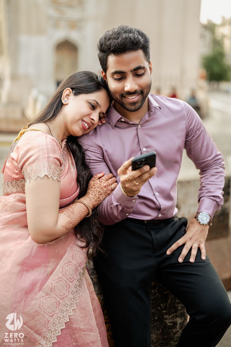 Couple in pink and purple attire sharing playful moments under architectural columns.