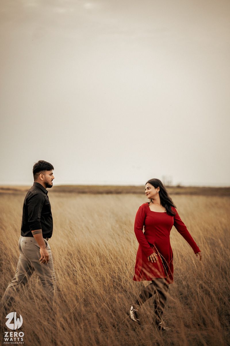 A couple in formal wear standing apart in a wheat field during golden hour.