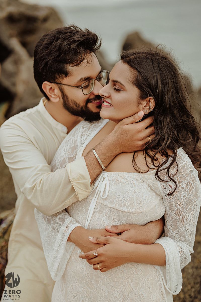 A romantic coastal photoshoot featuring a tender moment between a couple in white attire.
