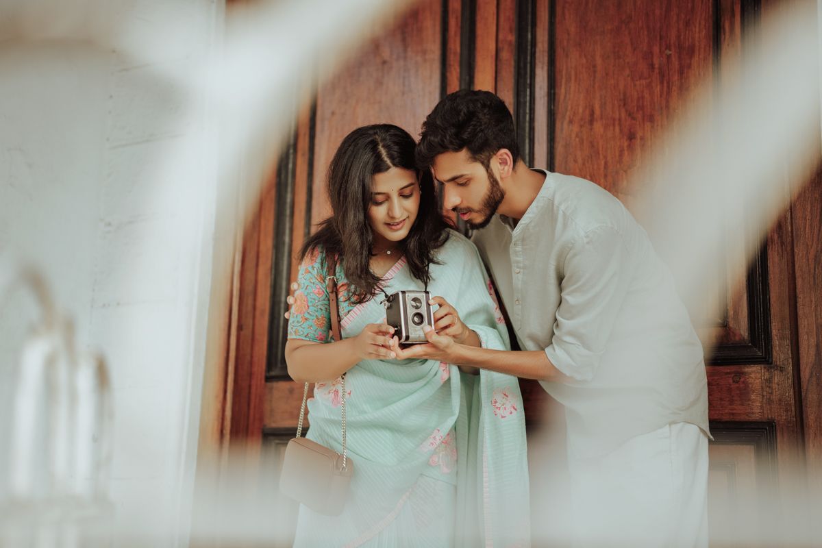 A couple in casual attire looks at a vintage camera together in a softly lit indoor setting.