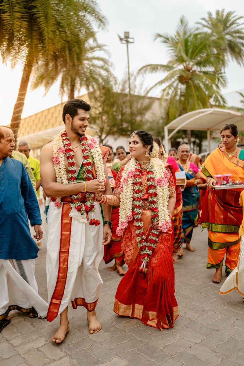 Traditional South Indian wedding procession with couple wearing red and white attire and flower garlands.