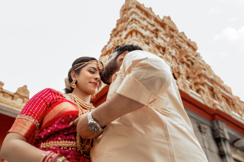 Intimate moment captured between couple in traditional attire against temple backdrop.