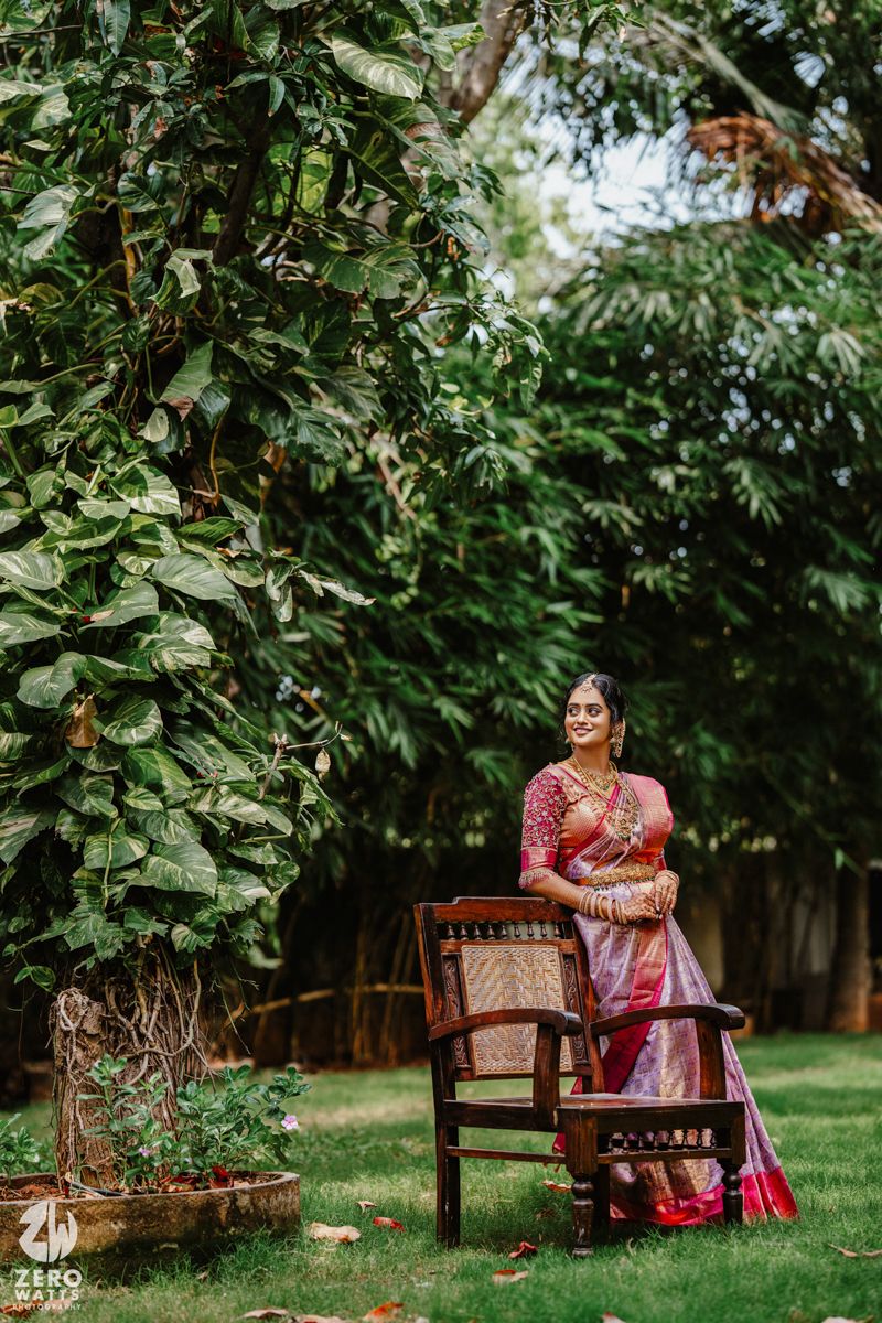 A stunning silk sari-clad figure poses elegantly on a wooden chair amid lush garden greenery.