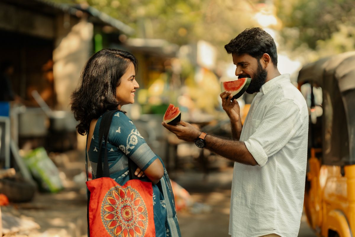 Two people share watermelon while standing on a bustling street in India.