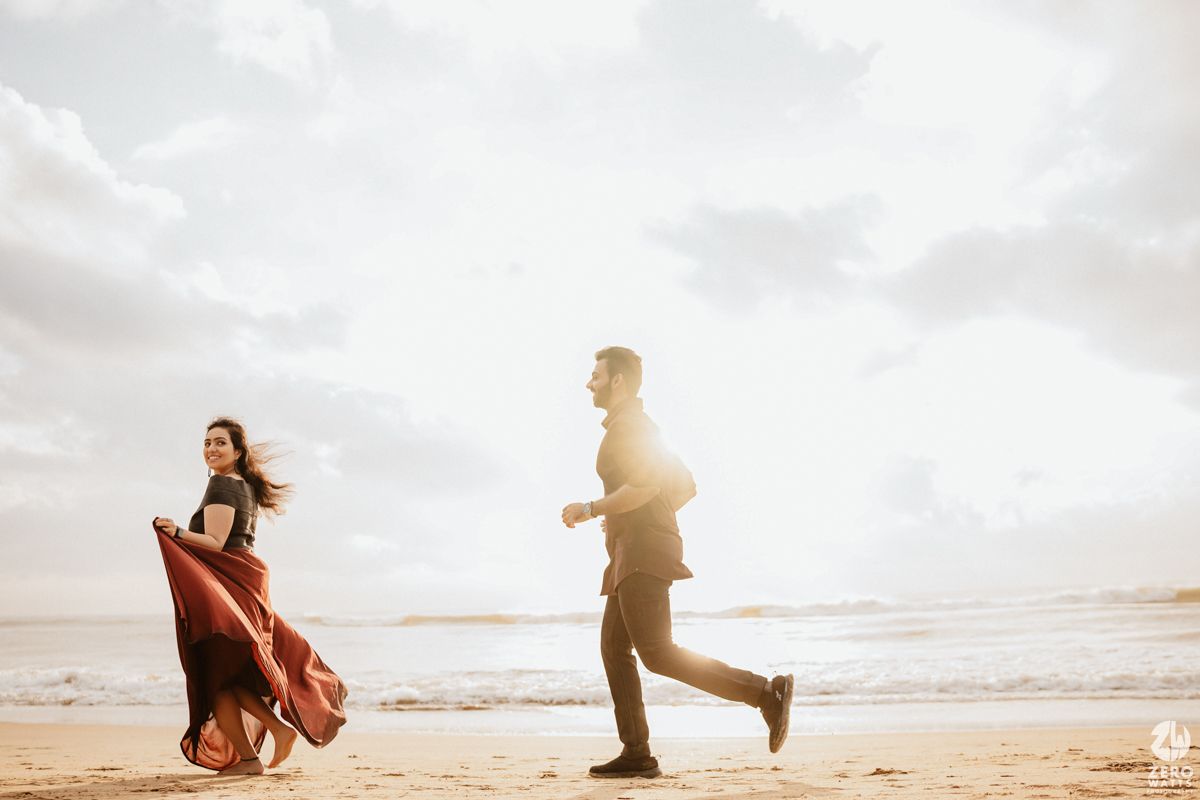 Two silhouetted figures playing and running along a sunset beach with flowing red dress and warm backlight.