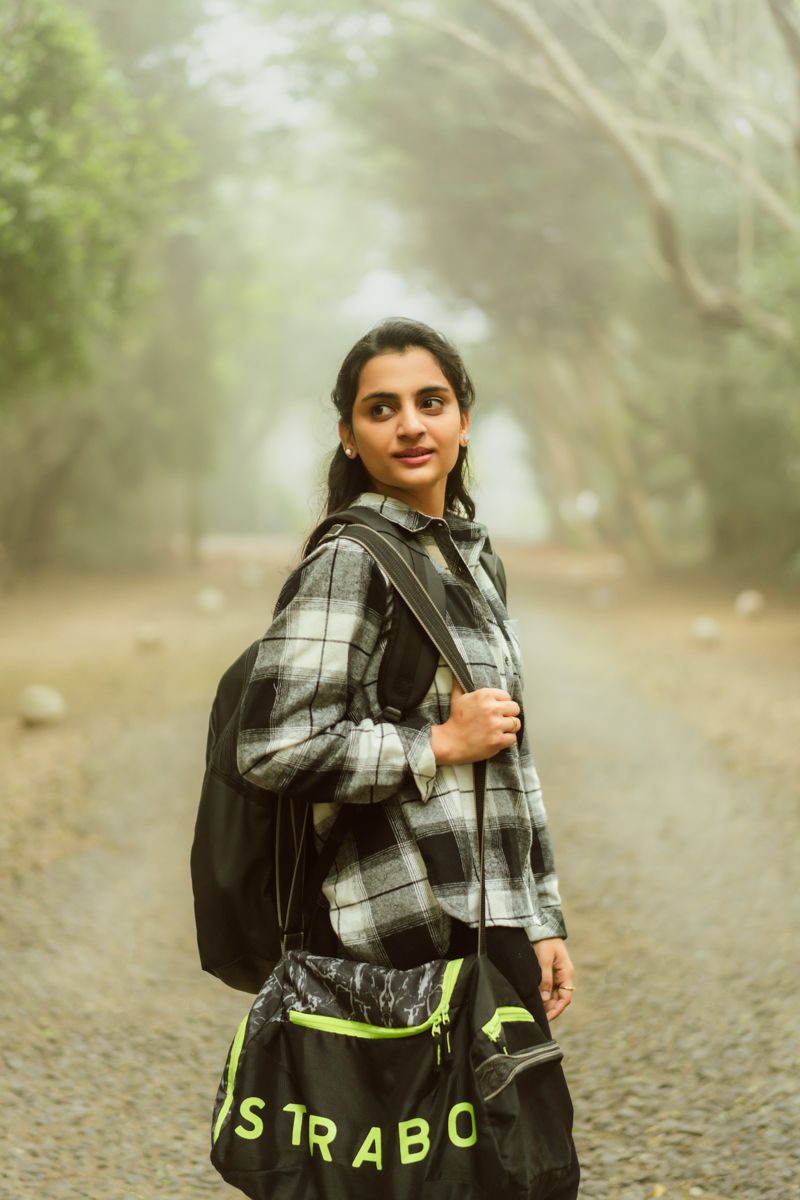 A person in a checkered shirt and backpack poses on a foggy forest trail with a large Strabo bag.