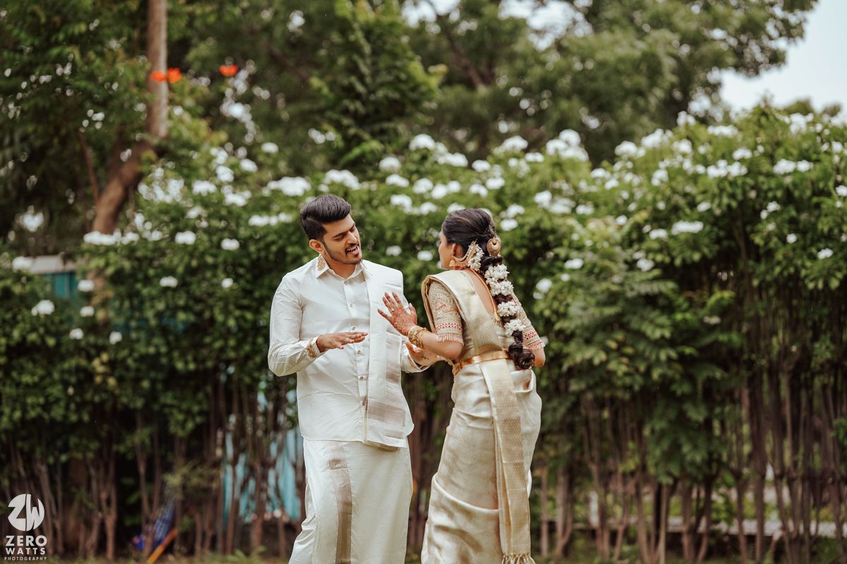 Three people in elegant wedding attire stand together under trees in a lovely outdoor garden setting.