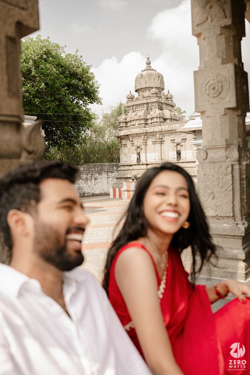 A couple in contrasting red and white outfits share joyful moments under ornate stone archways.