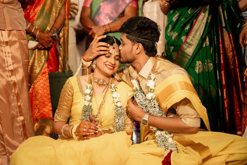 Traditional Indian wedding ceremony with couple wearing ornate yellow and gold outfits sharing intimate moment during celebrations.