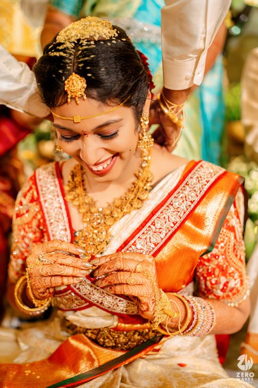 Bride adorned in traditional gold jewelry and red silk saree smiling during wedding ceremony.