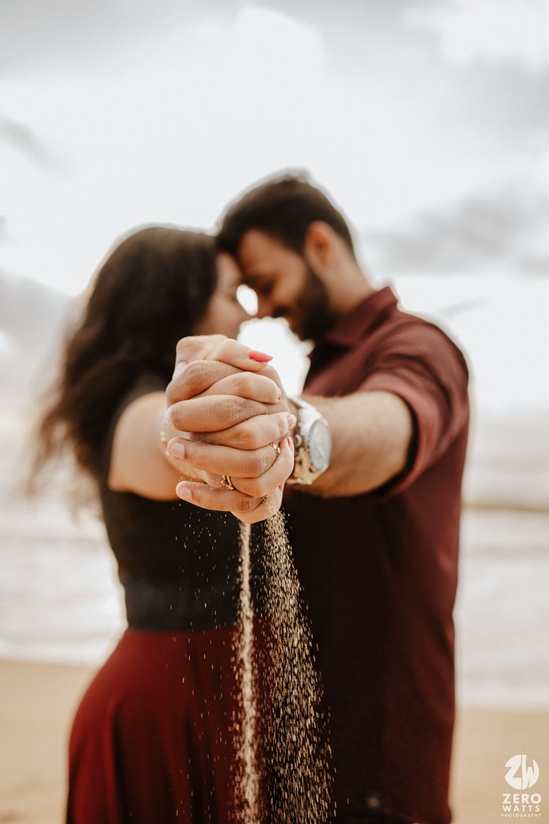 Romantic couple holding hands with sand falling between their fingers against dramatic cloudy sky.