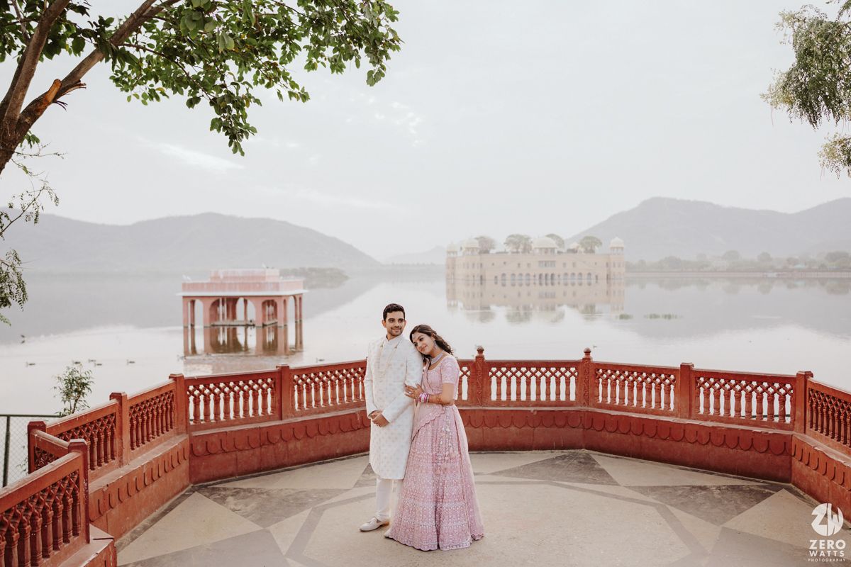A romantic couple stands on a red terrace overlooking a majestic palace and lake in Udaipur, India.