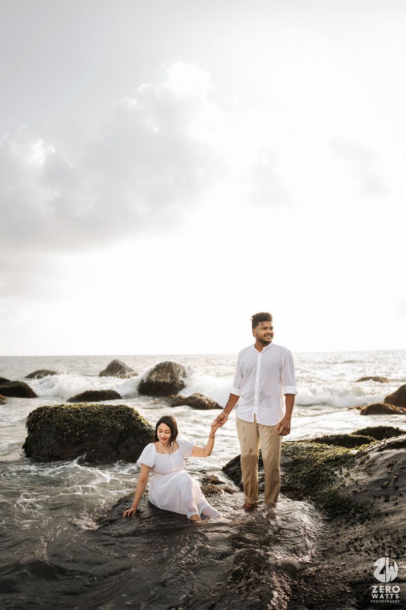 Couple on rocky beach shore with dramatic cloudy sky and ocean waves.