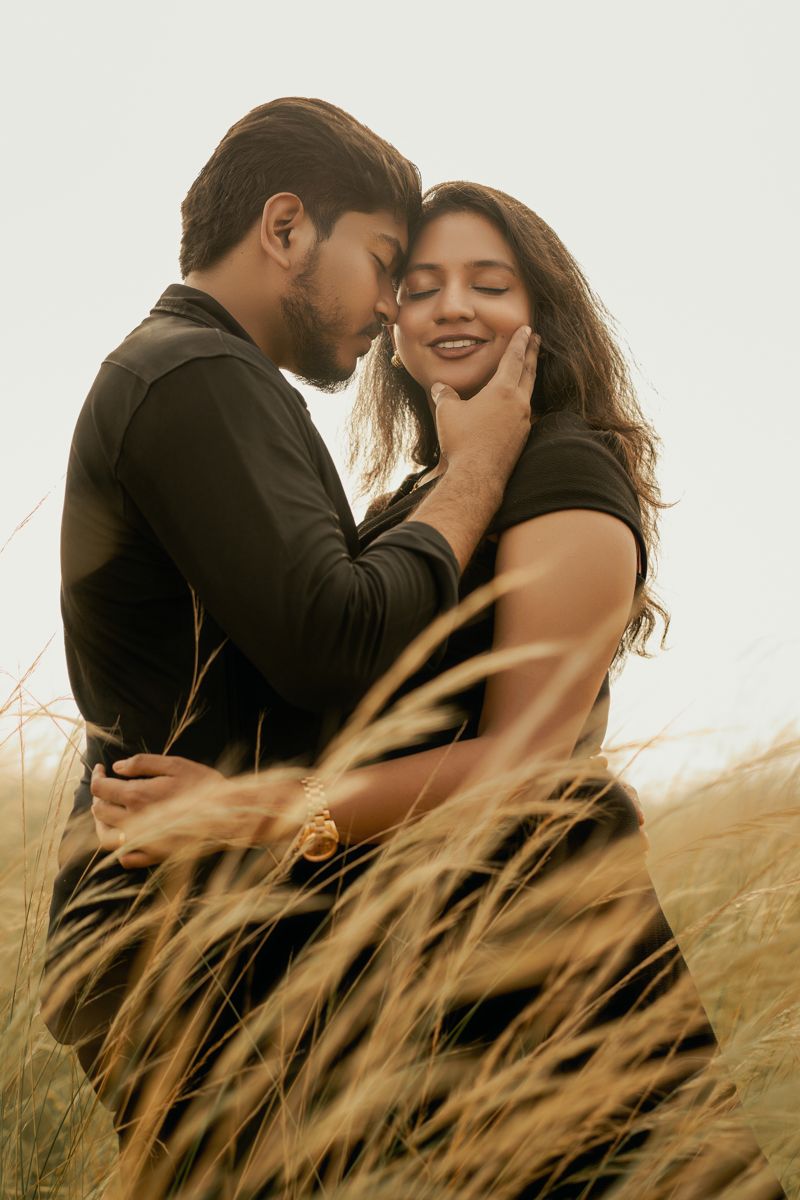Romantic couple embraces in golden wheat field at sunset wearing matching black outfits.