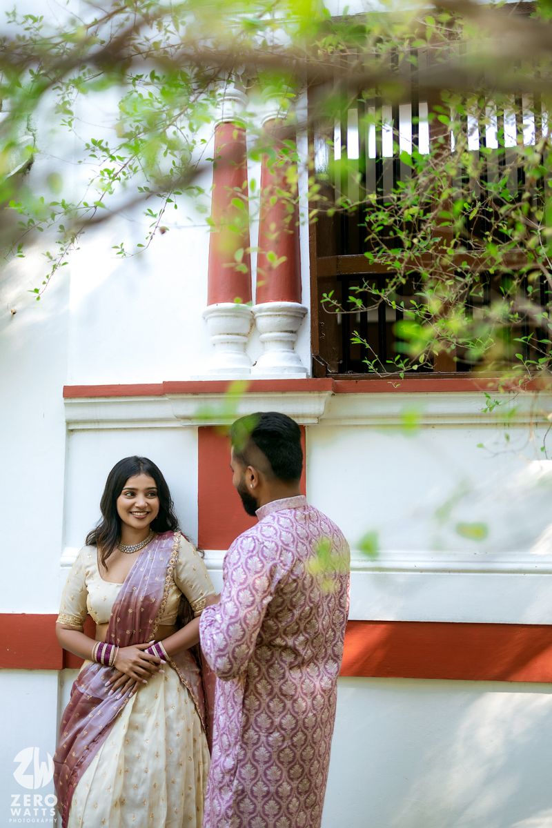 Couple in traditional attire standing by a white building with red accents and architectural details.