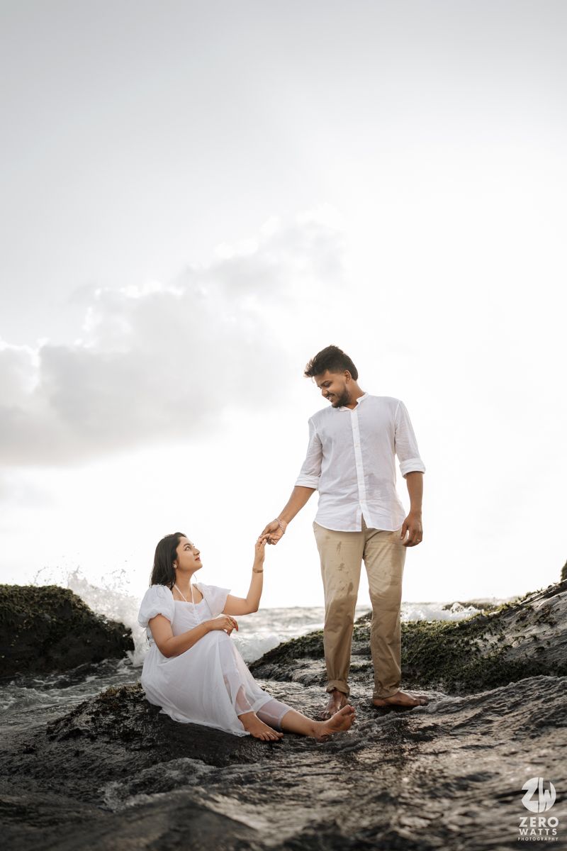 Couple posing on rocky beach during sunset with dramatic sky backdrop.