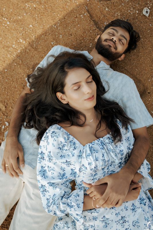 Couple laying on sandy ground wearing matching light blue and floral outfits.