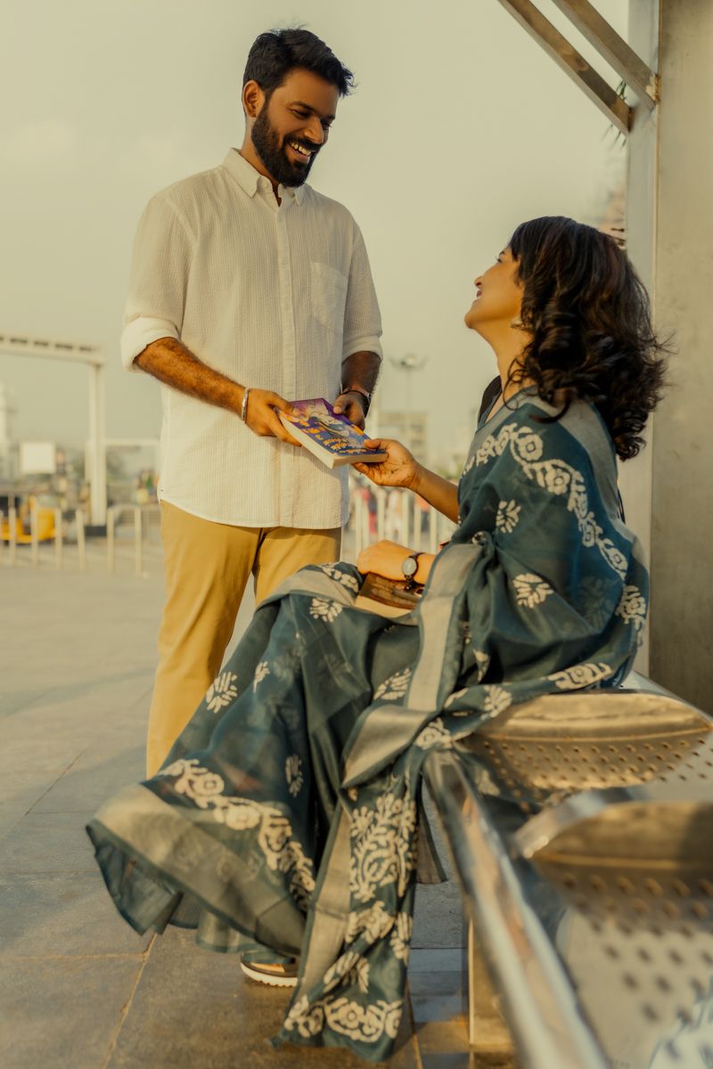 Two people sharing a moment on platform as person in blue saree reads book during golden hour.