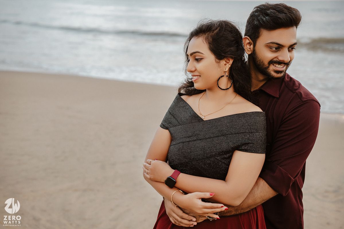 A couple embraces on a beach while sharing a joyful moment together during a romantic photoshoot.