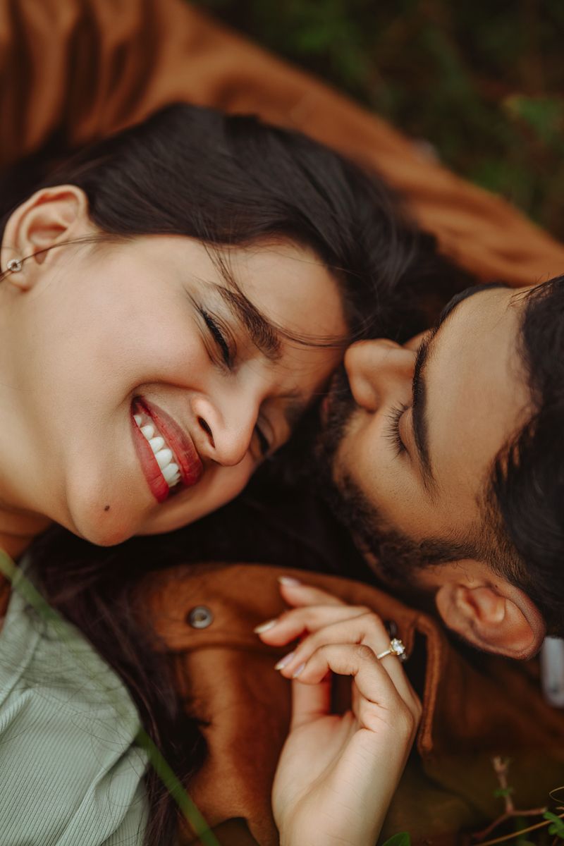 Close-up shot of couple lying down and smiling intimately together on brown blanket.
