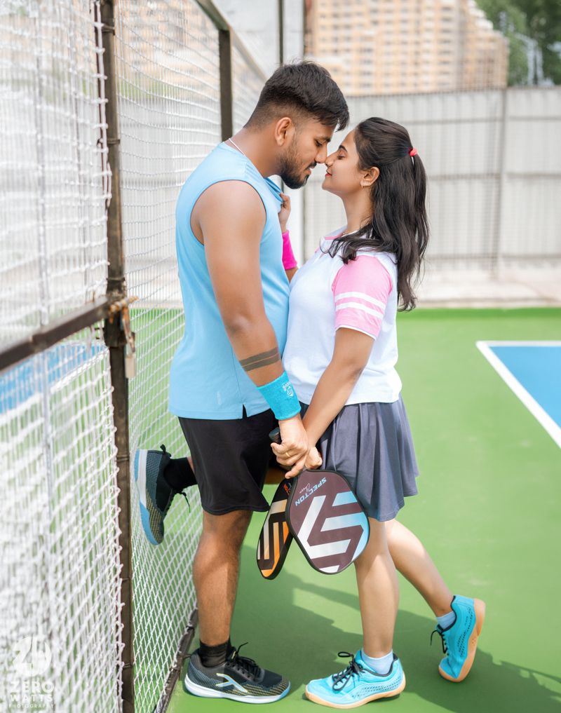 Athletic couple sharing an affectionate moment against the fence of a pickleball court.