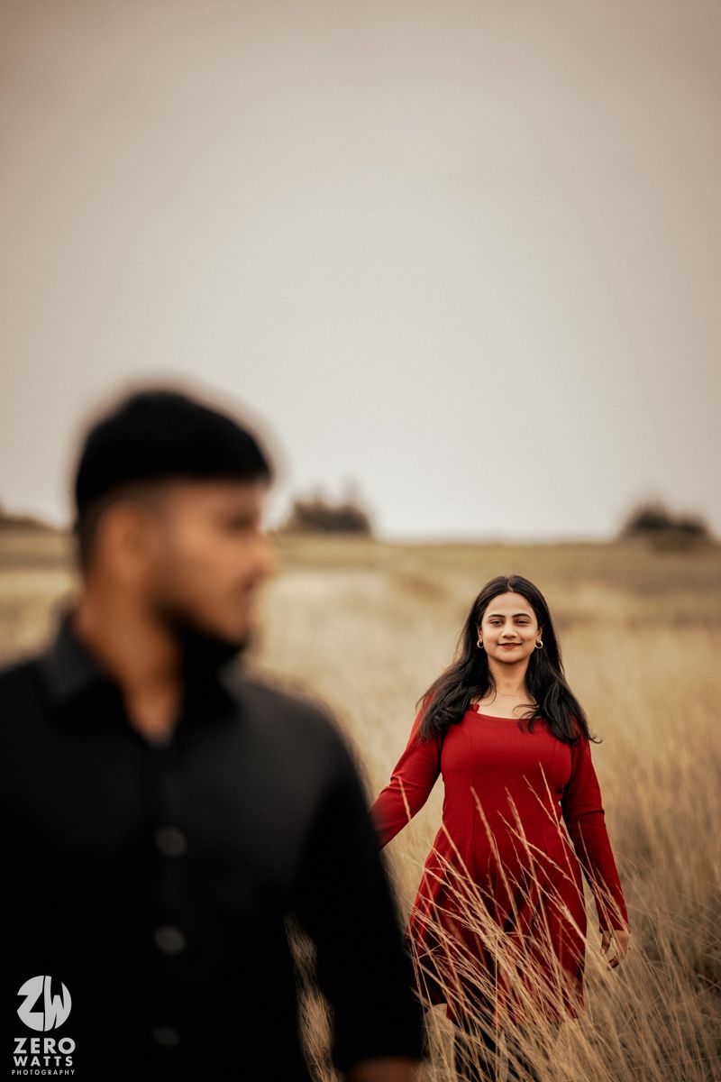 A couple in contrasting outfits standing among tall grasses in warm lighting.