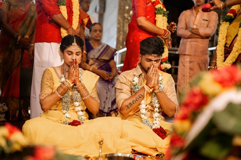 Couple in traditional Indian wedding attire praying together during a vibrant wedding ceremony.