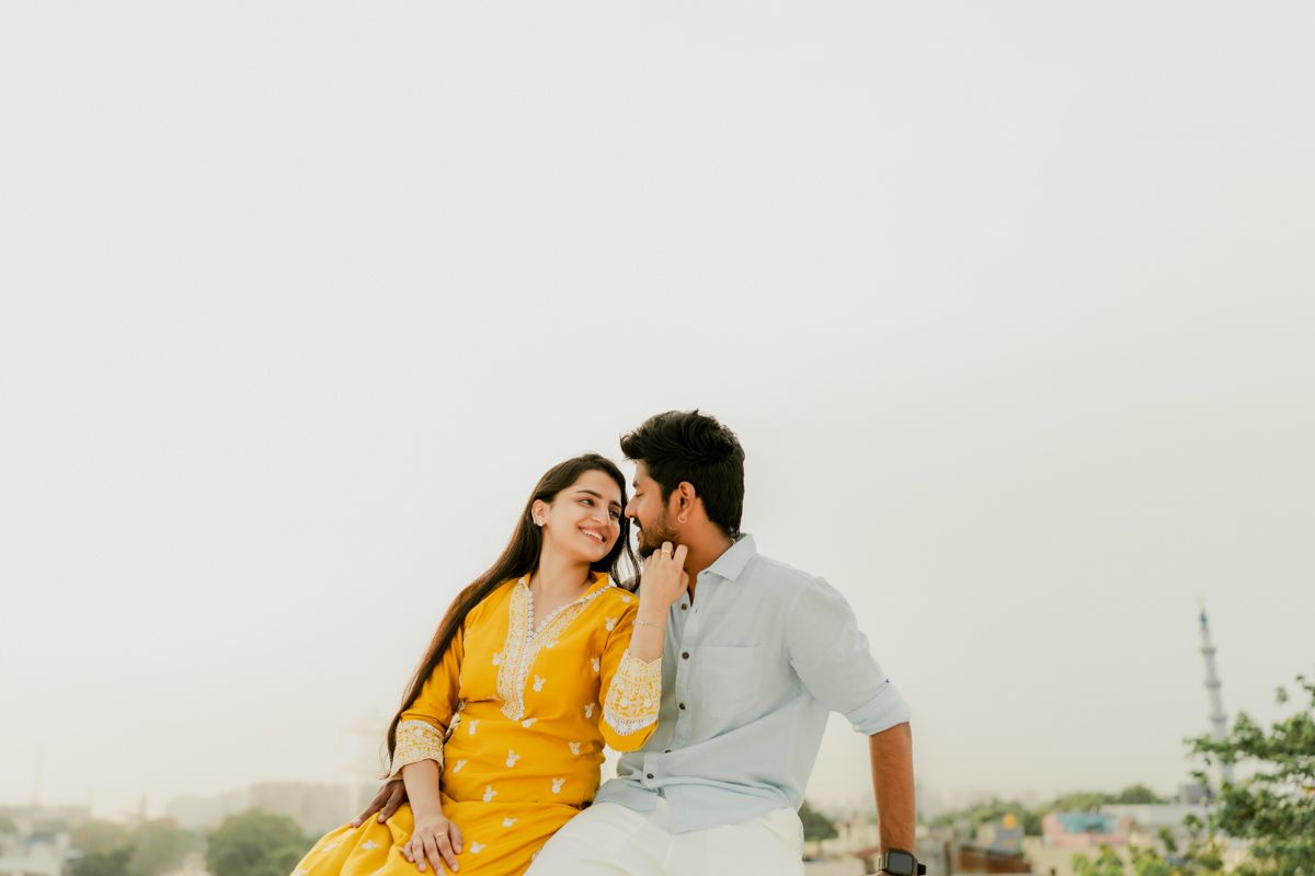 A romantic moment captured between a couple dressed in yellow and gray sitting together outdoors.