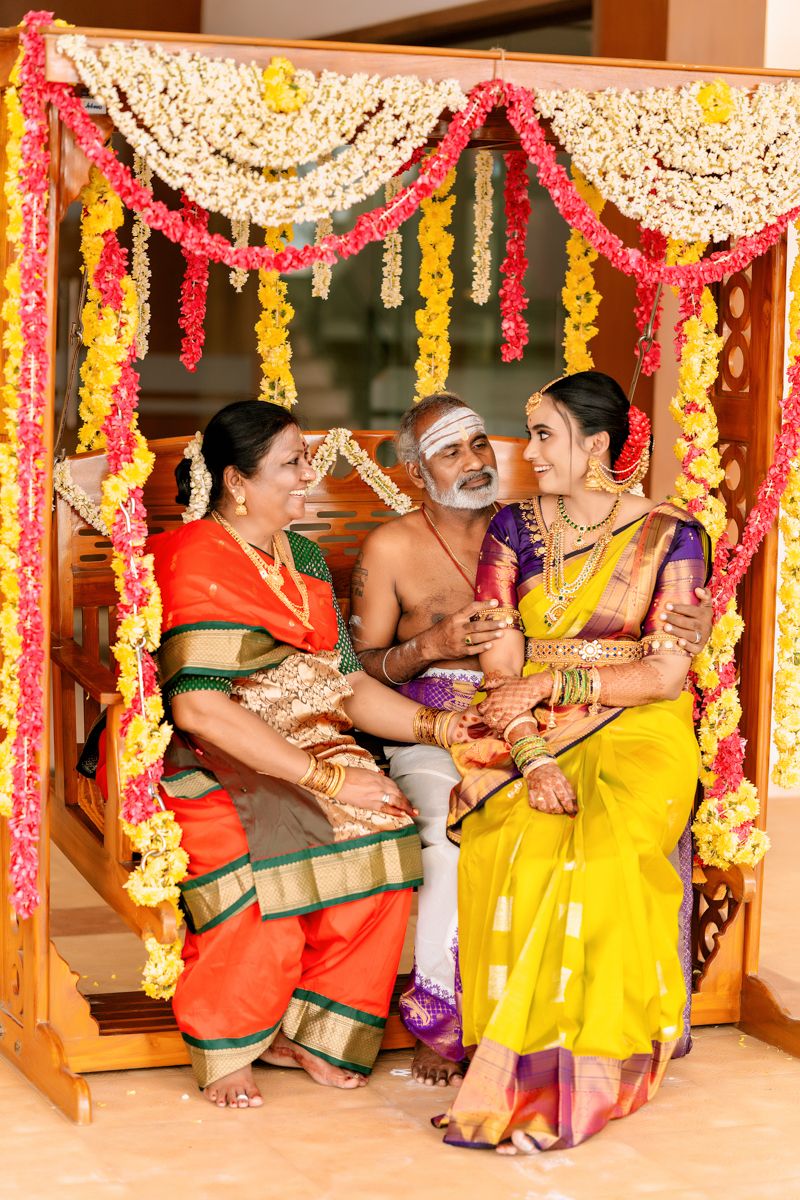 Traditional Indian ceremony with colorful floral decorations and people in traditional attire seated on a wooden swing.