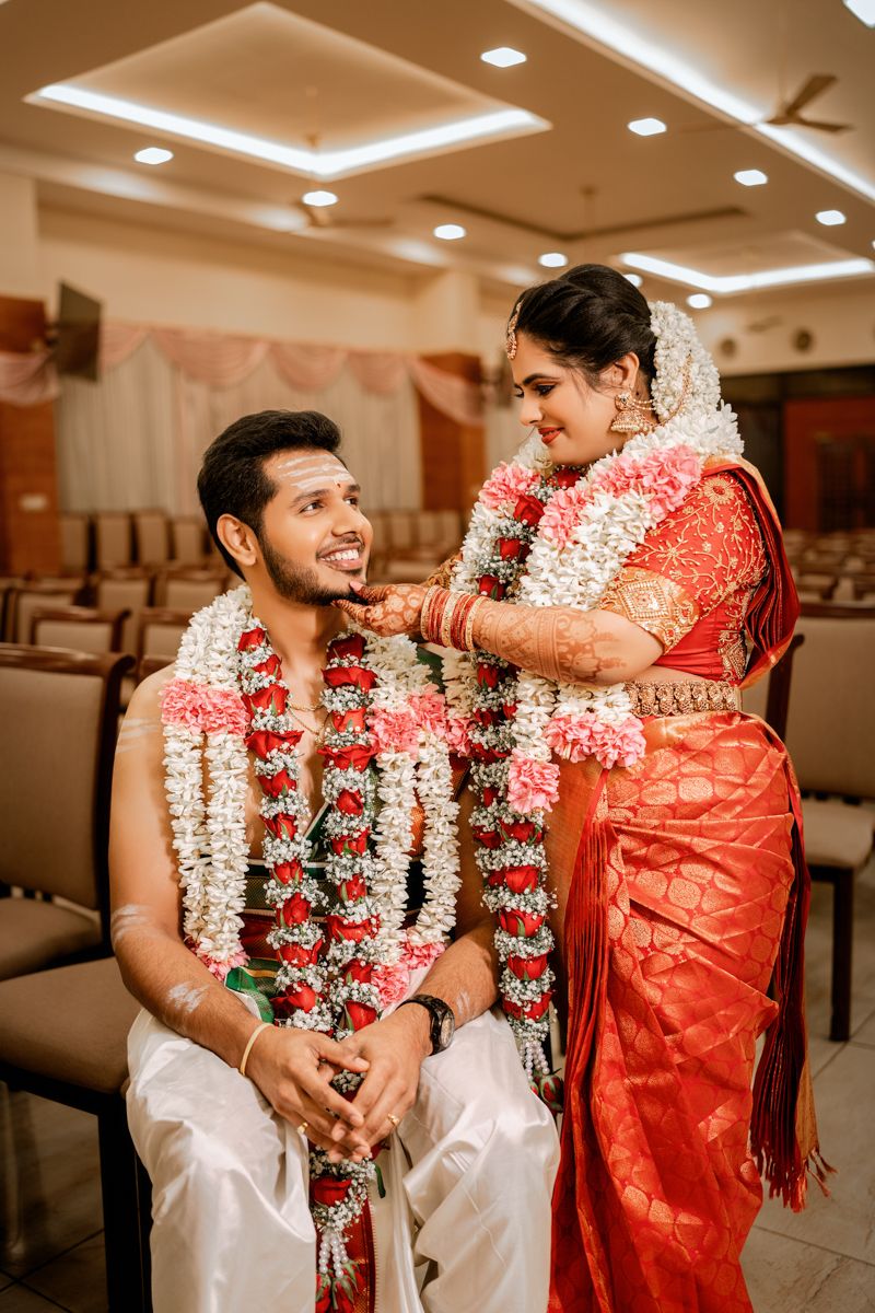 A traditional South Indian wedding ceremony with the couple wearing garlands and the bride in a vibrant red silk saree.