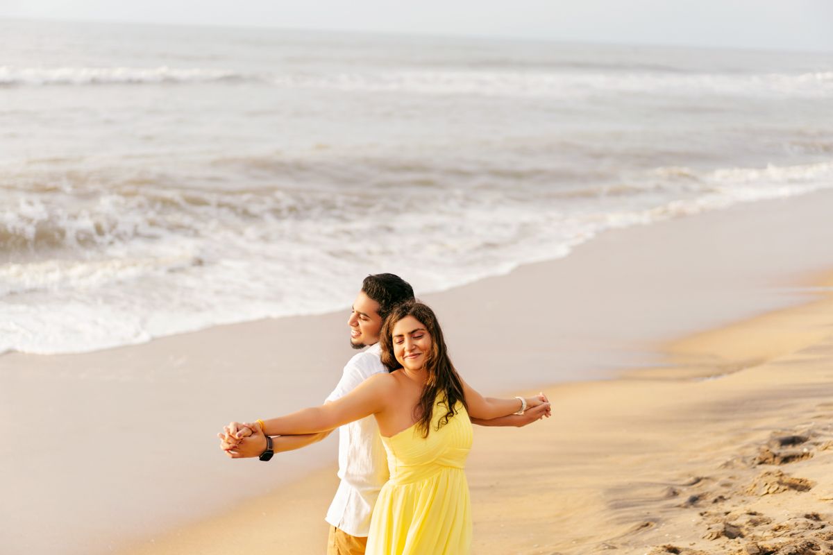 Two people in bright clothing enjoying a carefree moment together on a sandy beach with waves in the background.