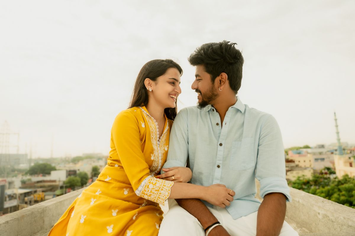 A romantic couple in complementary yellow and mint outfits share a joyful moment on an urban rooftop.