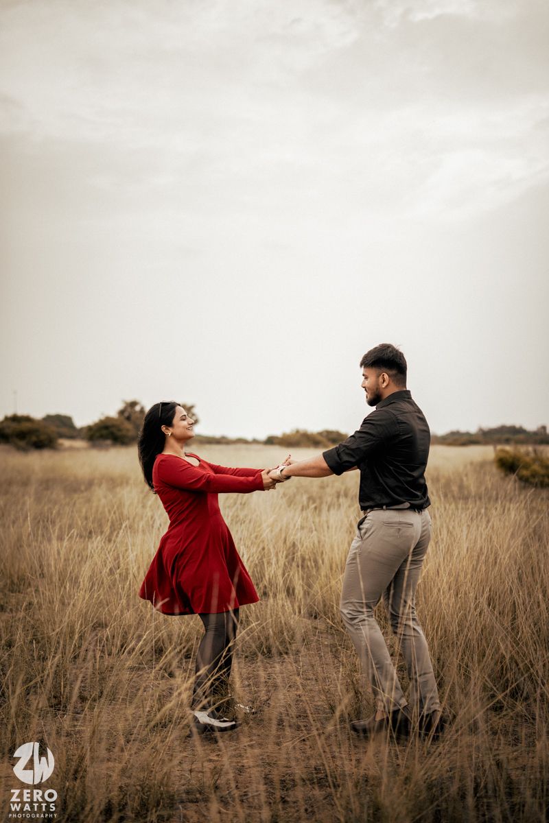 Couple dancing playfully in a golden field of tall grass at sunset.