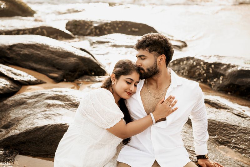Intimate moment captured between couple on rocky beach shore.