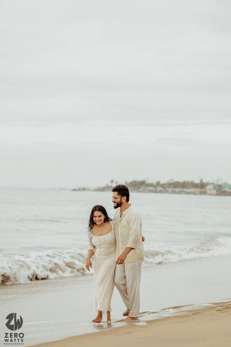 Couple walking together on beach shore during overcast day.
