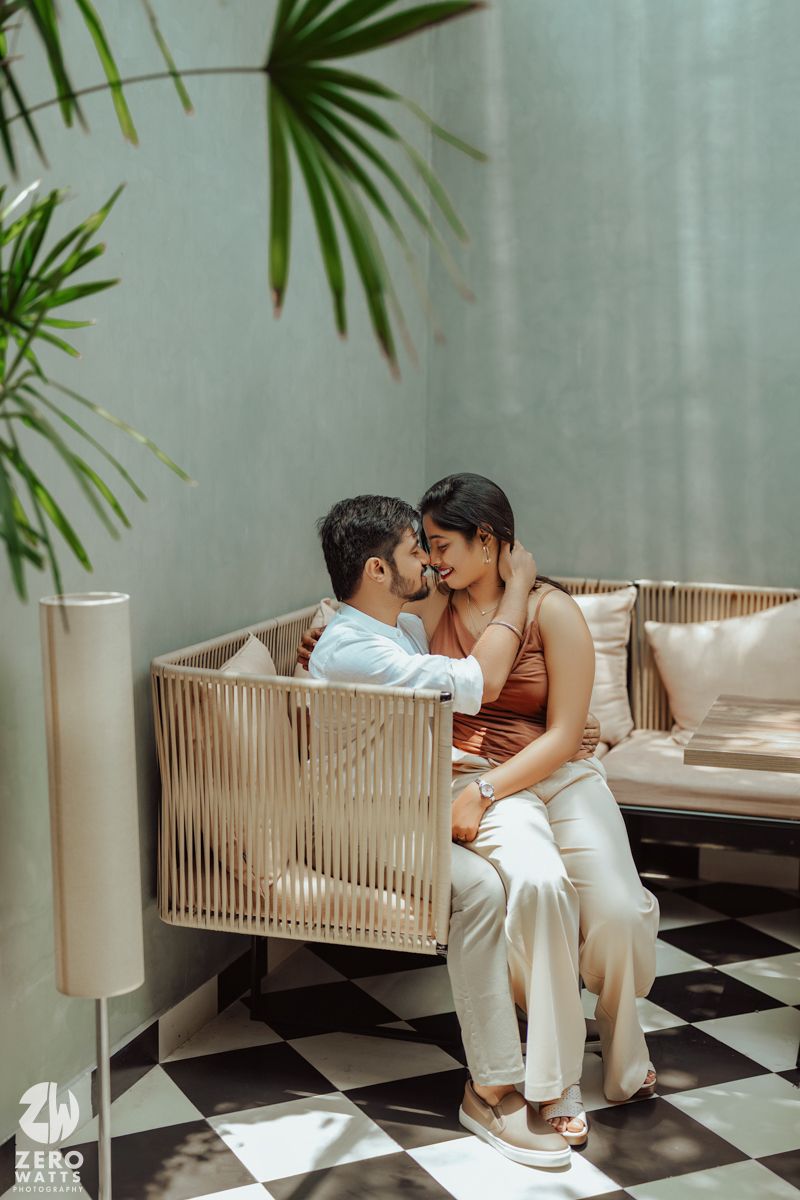 Intimate moment shared on woven chairs in an elegant indoor space with palm leaves and checkered floors.