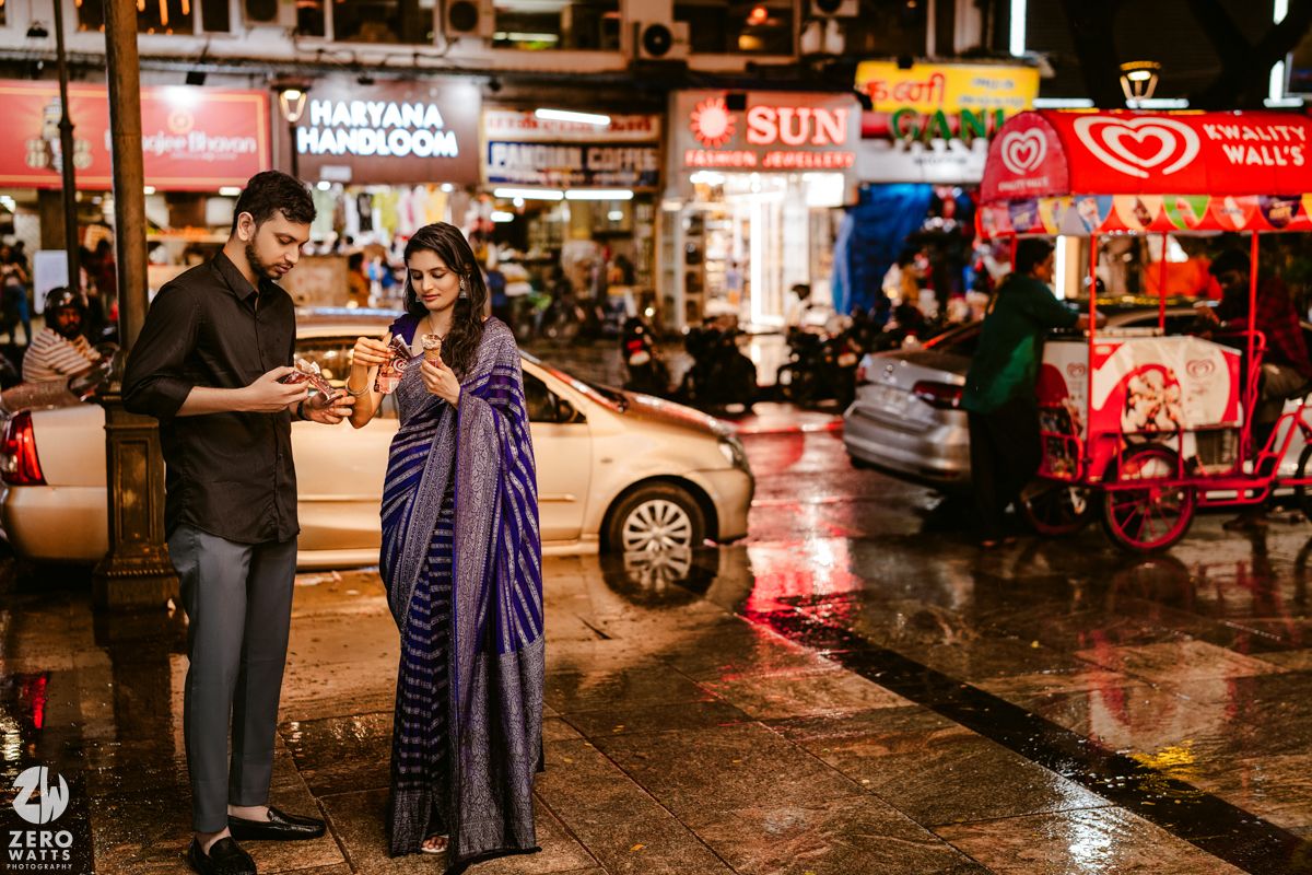 A nighttime street scene with couple sharing conversation amid city lights and rain.