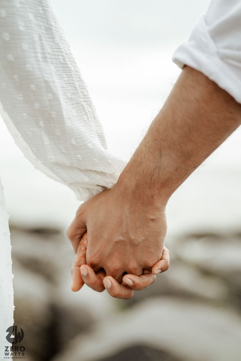 Close-up shot of two people holding hands, wearing white clothing against a bright background.