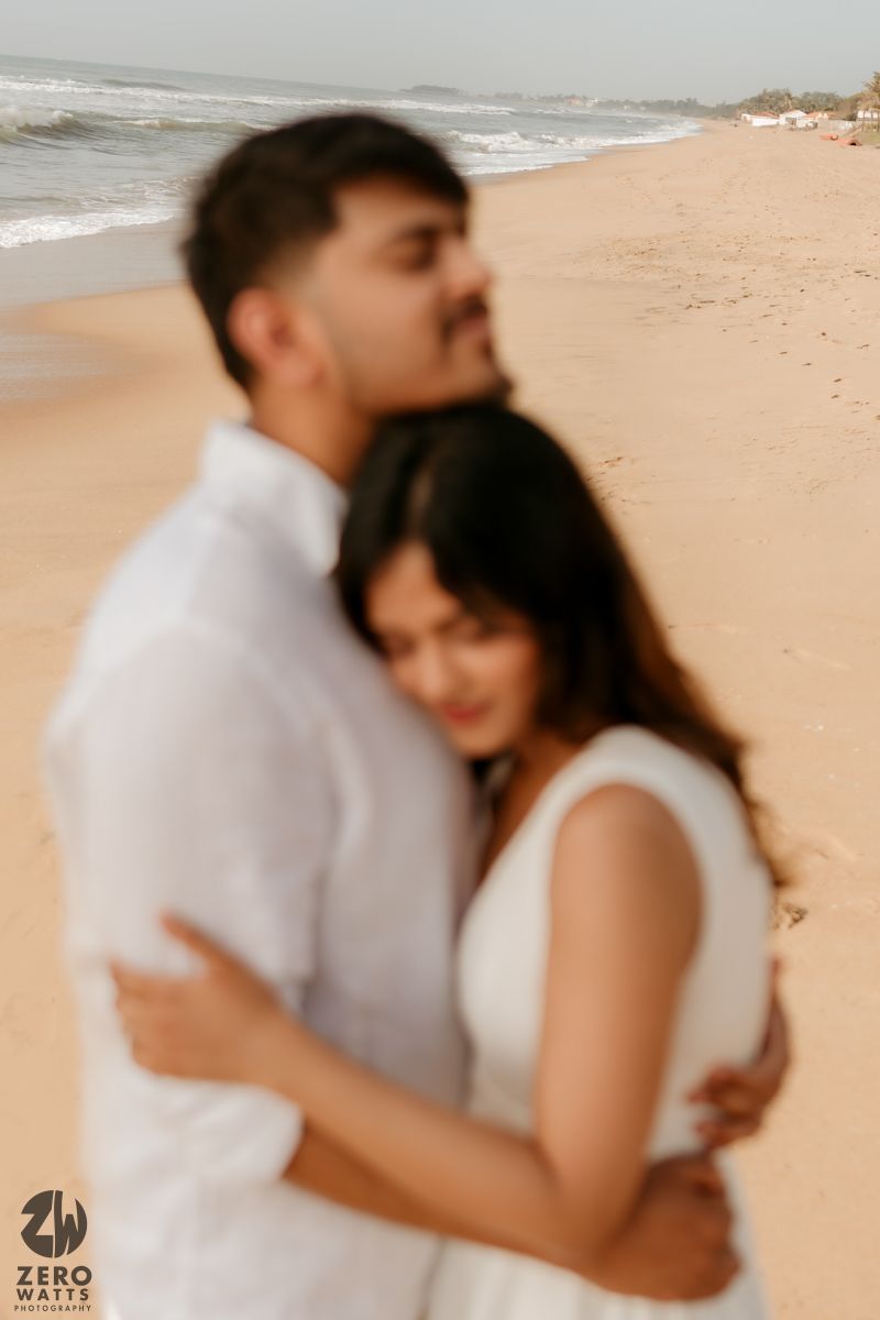 Intimate beachside portraits of couple embracing in white outfits against sandy backdrop.