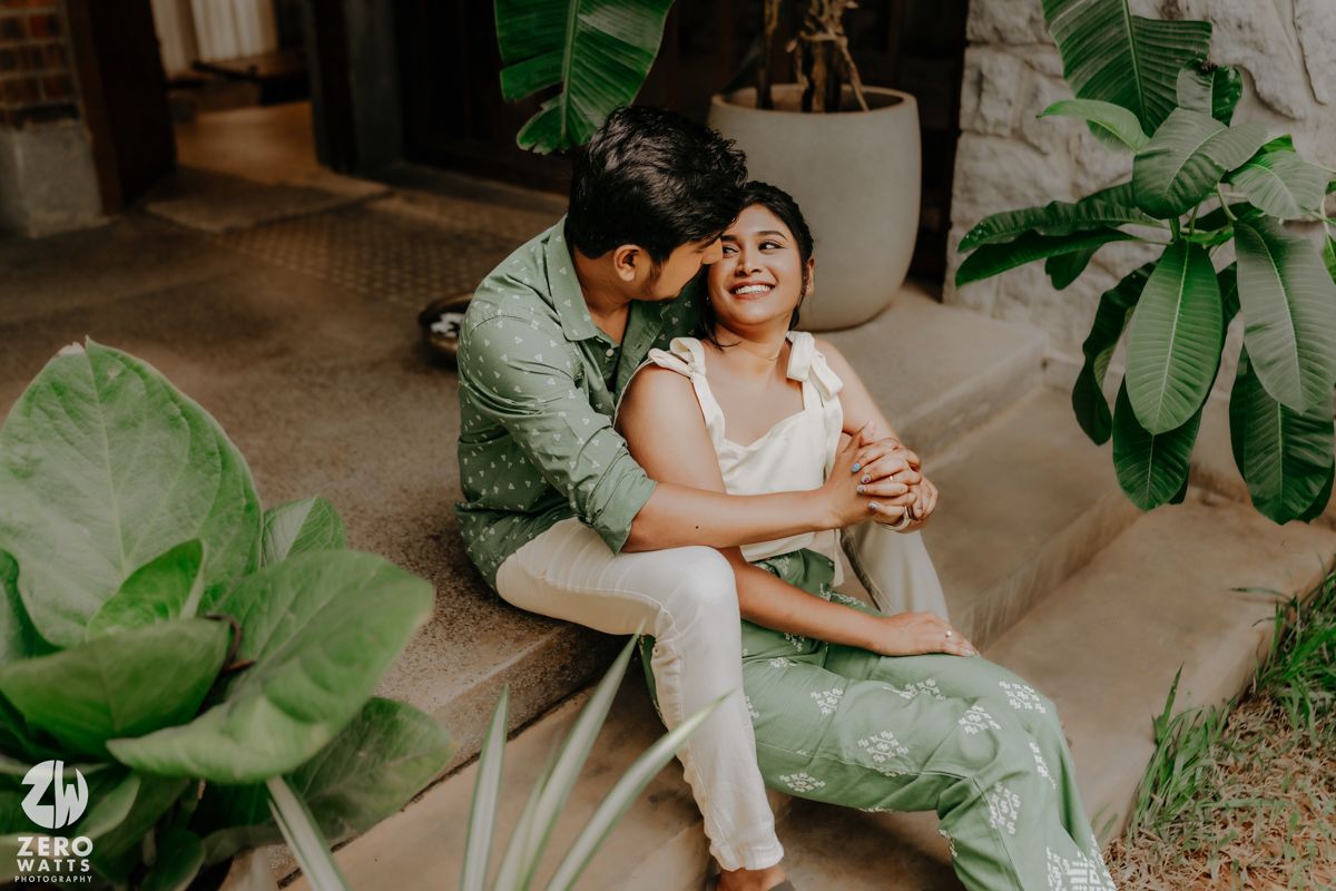 Intimate couple sharing tender moment while relaxing together among green tropical plants in indoor setting.