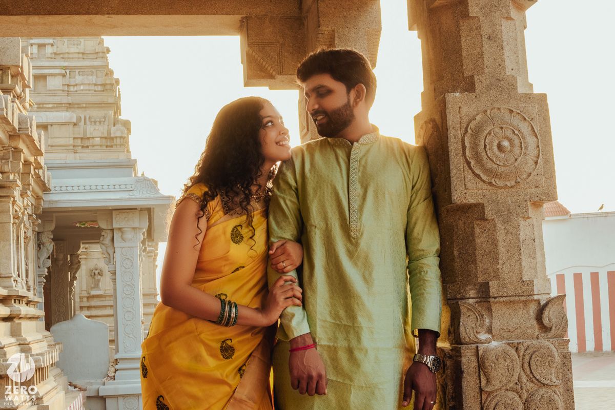 A couple in traditional Indian attire share an intimate moment at a temple during golden hour.