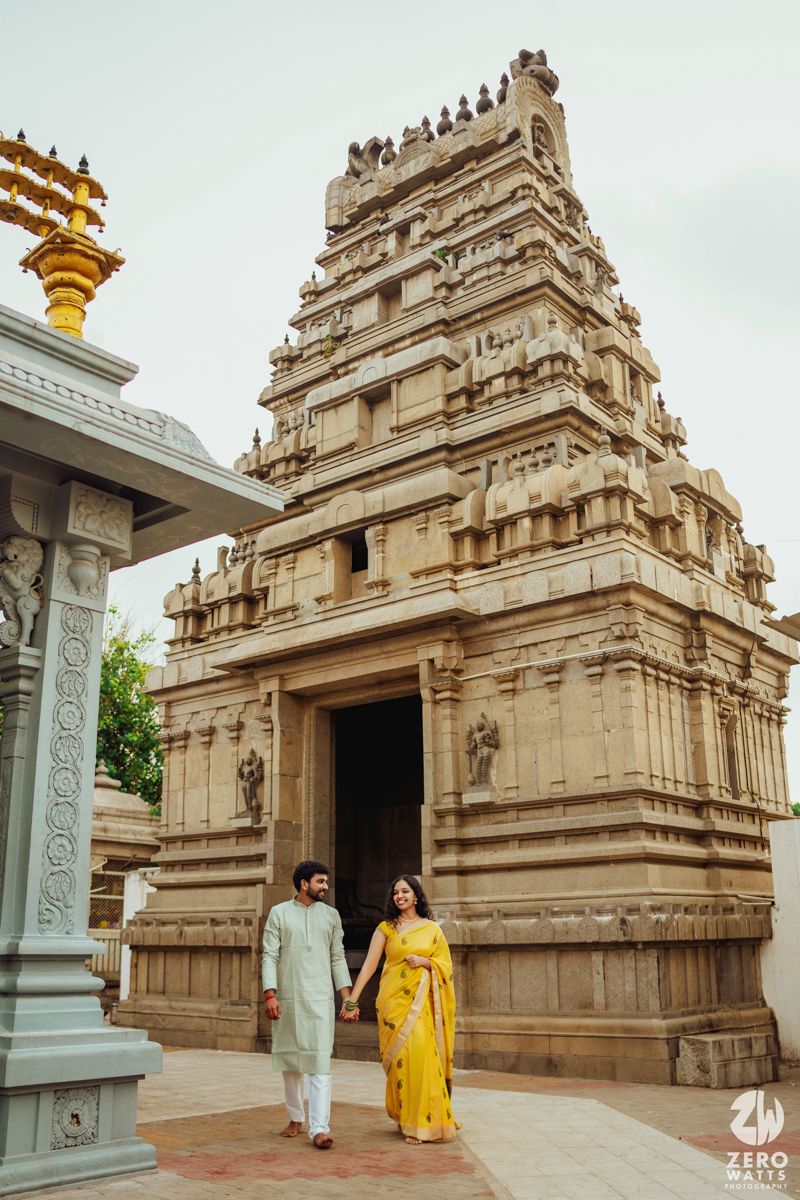 Traditional South Indian temple architecture with ornate carved stone gopuram and couple in traditional attire walking outside.