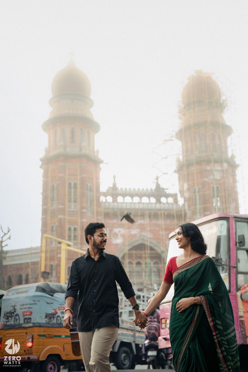 A couple stands holding hands in front of ornate mosque towers in an urban setting.
