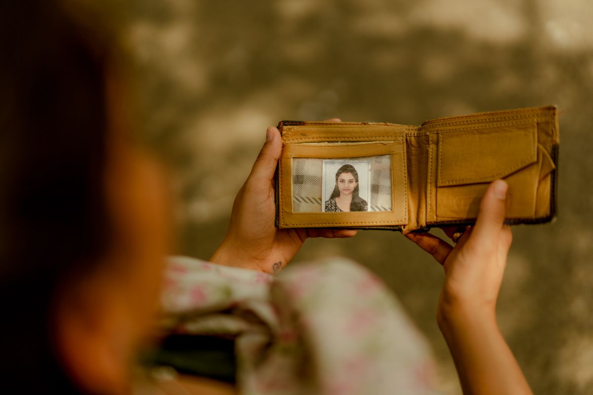 Hands holding open a brown leather wallet displaying an ID photo.
