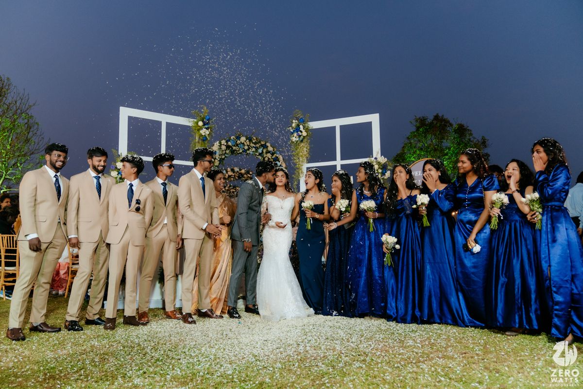 Wedding party in blue dresses and beige suits poses for a photo under a stormy evening sky.