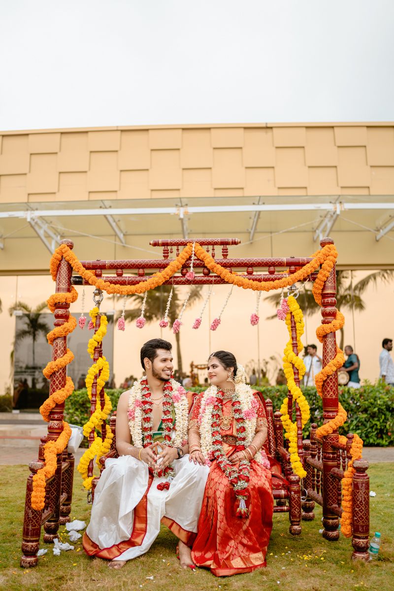 Traditional Indian wedding ceremony under a decorated mandap with orange and red marigold flowers and draped fabric.