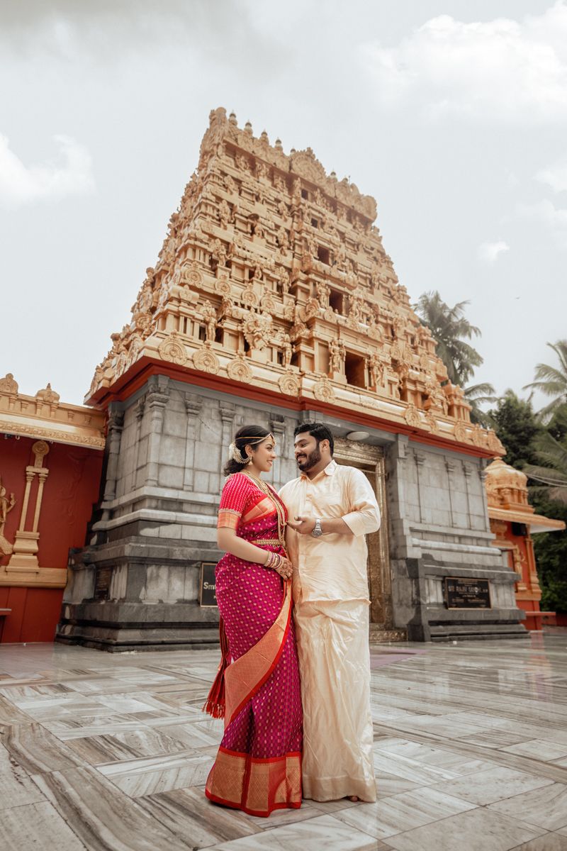 Traditional wedding couple poses in front of ornate temple gopuram architecture in South India.